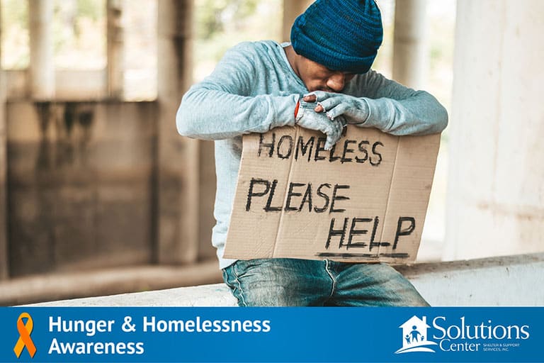 A homeless man sitting on a crate holding a cardboard sign.